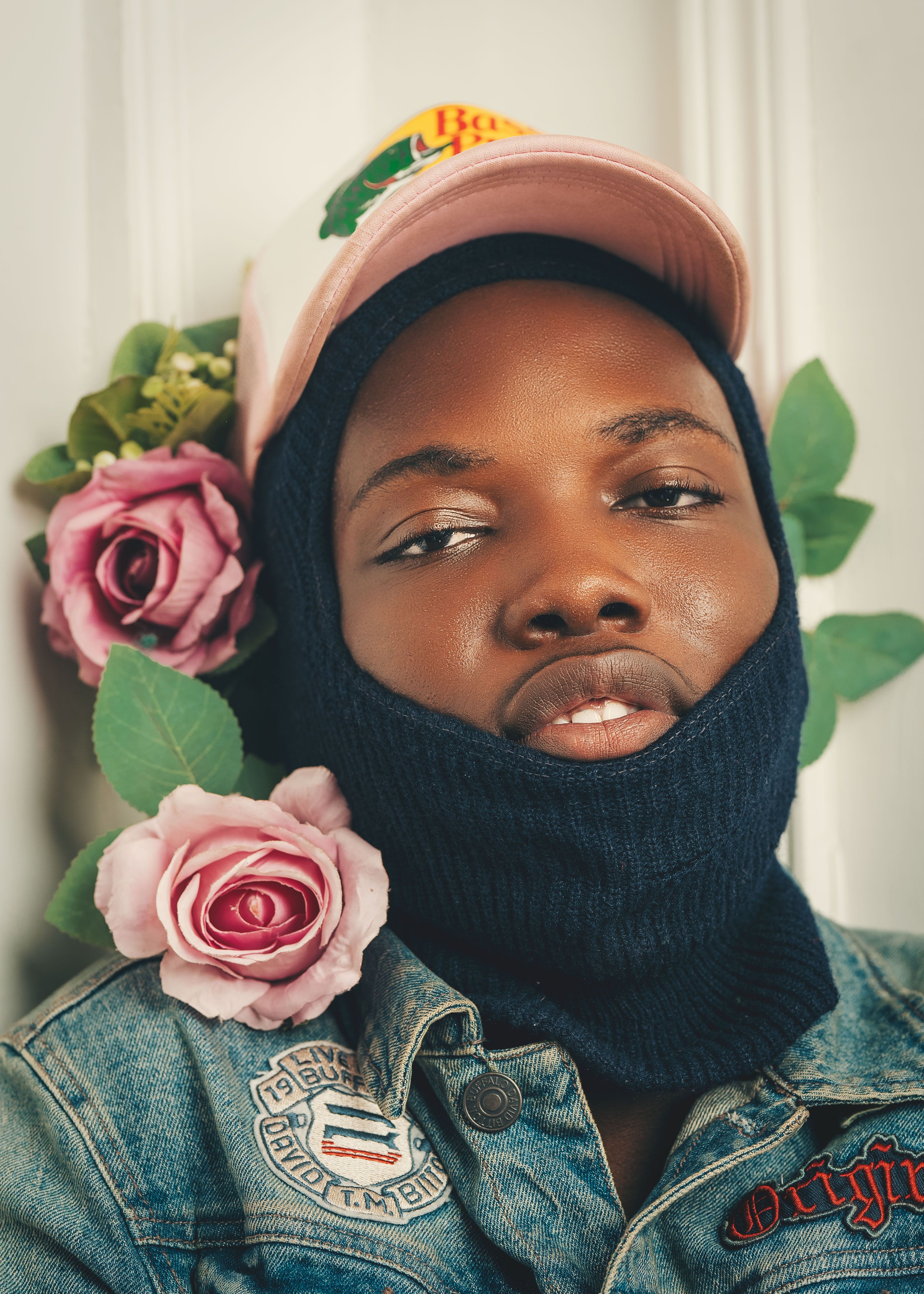 Young man in a pink cap, balaclava and denim with roses.