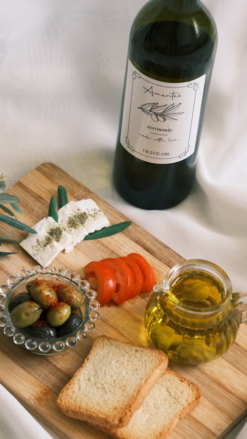 A wooden cutting board with olives, bread and wine