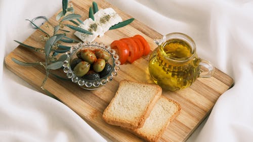 A wooden cutting board with bread, olives and olive oil
