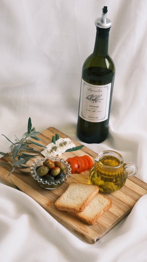 A bottle of wine, bread and olive oil on a wooden cutting board