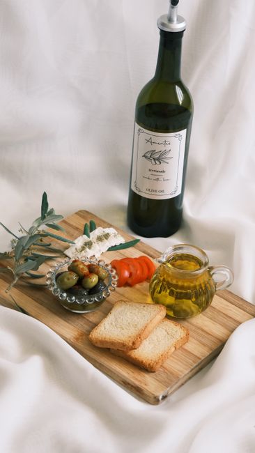 Elegant still life featuring olive oil, bread, and olives on a cutting board.