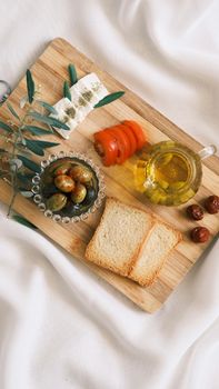 Top view of Mediterranean ingredients with bread, olives, and olive oil on a wooden tray.
