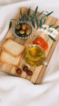 Aesthetic still life with olives, olive oil, bread, and vegetables on a wooden board.