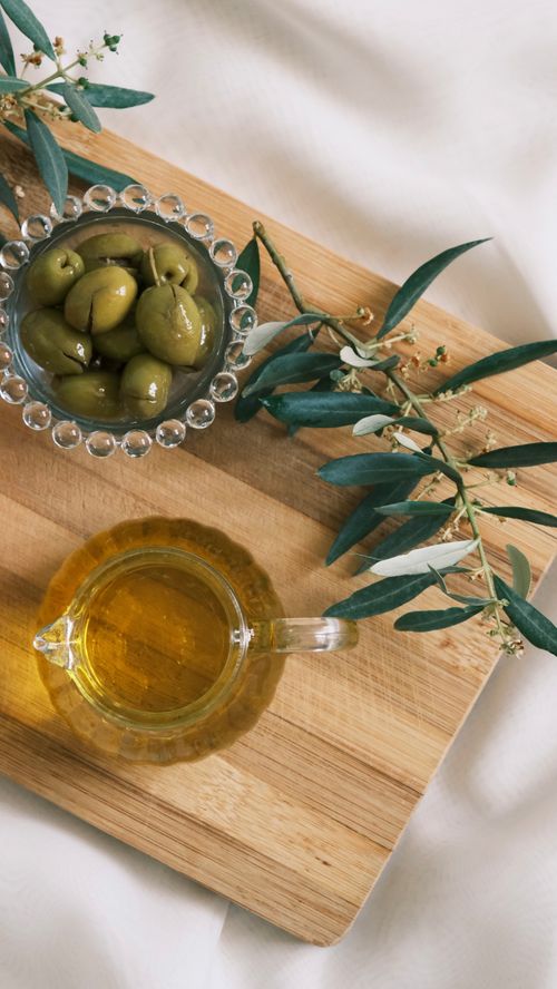 Free Top-down view of olives and olive oil on a cutting board with olive branches. Stock Photo