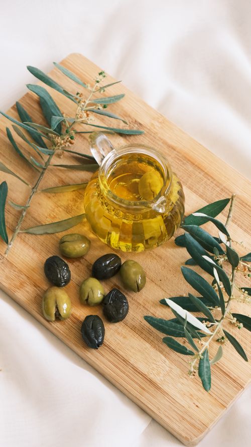 Free Cozy setup featuring olives and olive oil on a wooden board with olive branches. Stock Photo