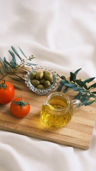 Top view of fresh olives, tomatoes, and olive oil on a wooden tray.