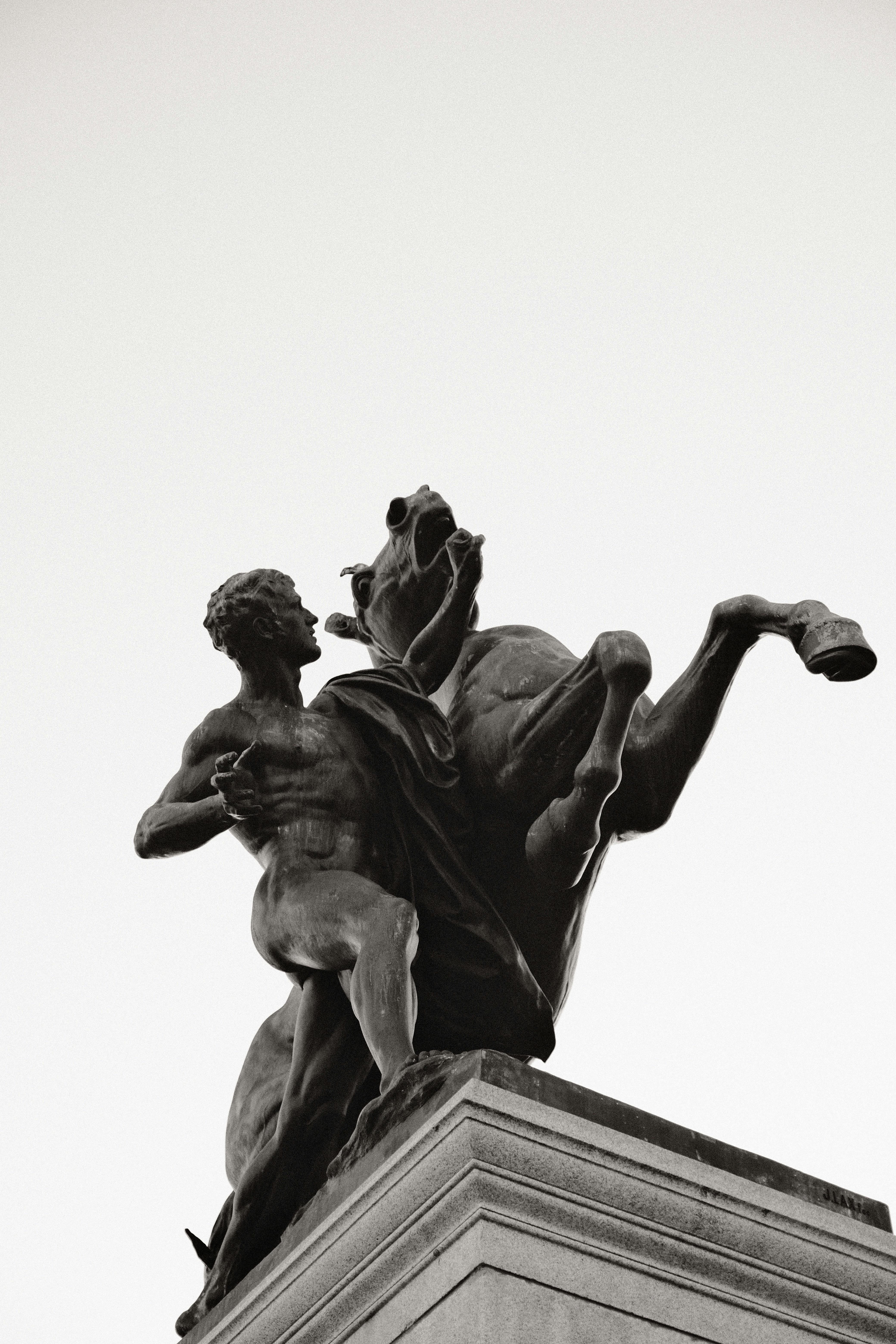 Monochrome statue of man and horse in urban setting, low angle.