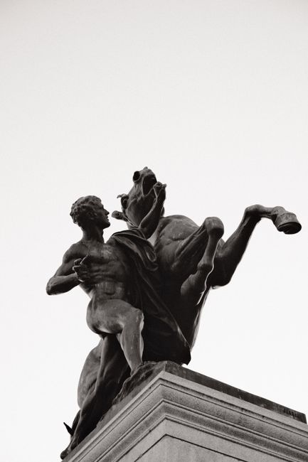 Monochrome statue of man and horse in urban setting, low angle.