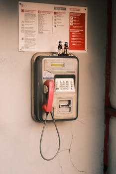 A vintage wall-mounted payphone with red handset and beer bottles on top.
