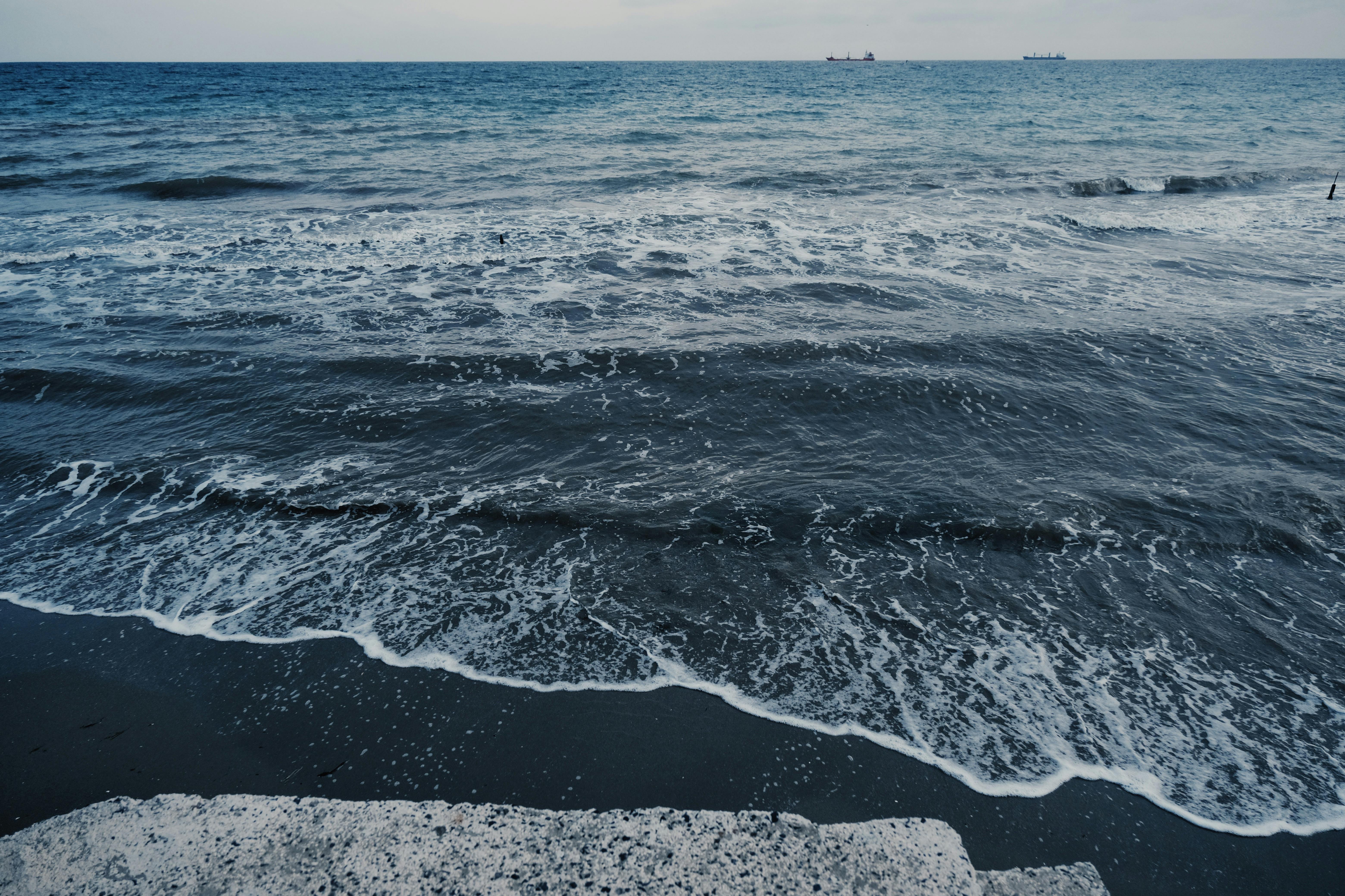 Peaceful ocean waves gently hitting a sandy beach under a cloudy sky, creating a tranquil seascape.