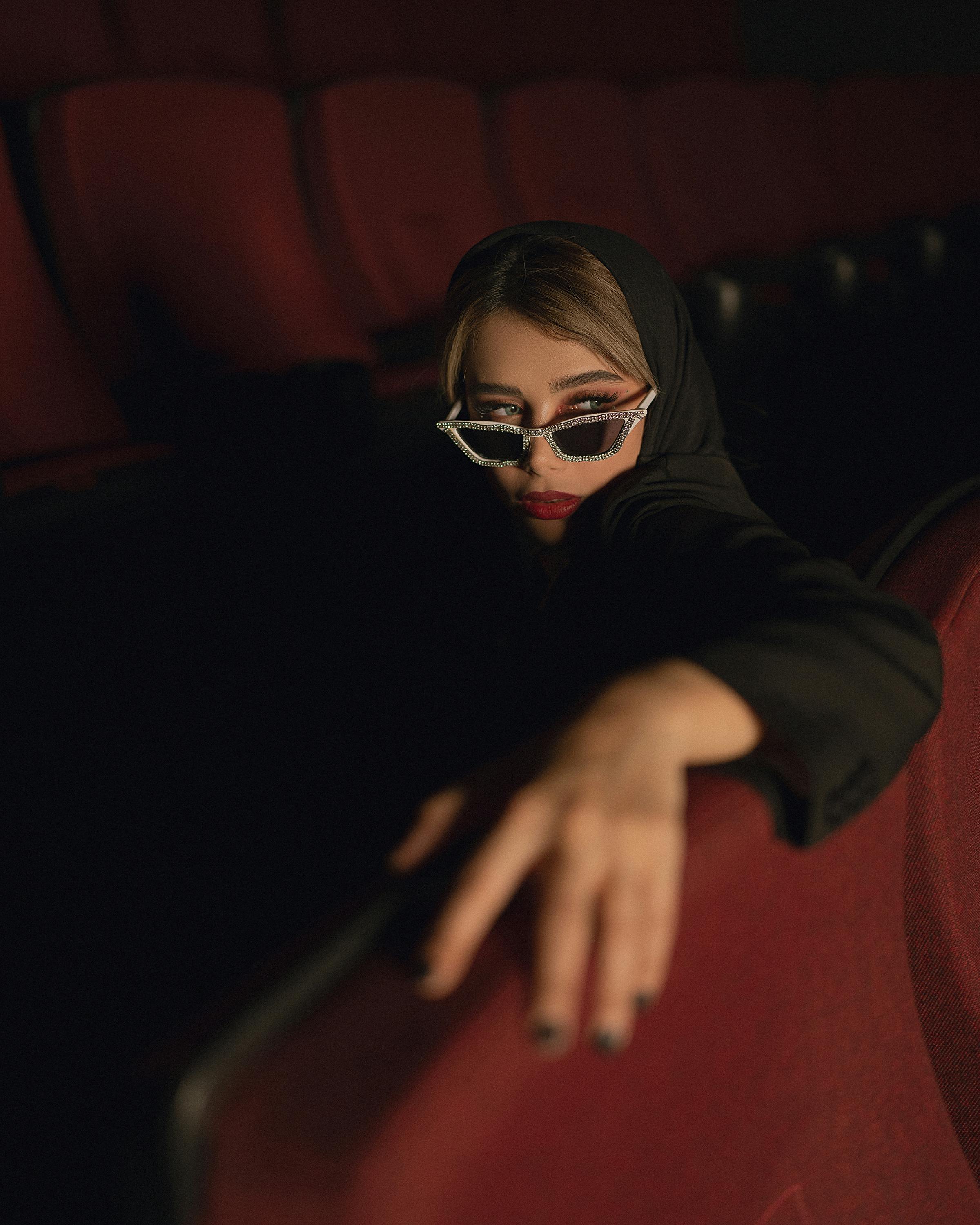 Free Elegant woman posing stylishly in red cinema seats, wearing sunglasses and headscarf. Stock Photo
