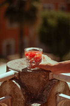 A hand holding a refreshing strawberry cocktail on a sunny balcony in Lido, Italy.