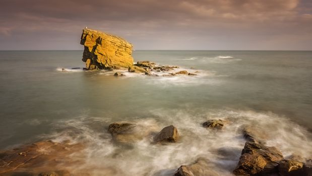 Captivating view of a rocky coastal formation illuminated by sunset light, with waves gently lapping the shore.