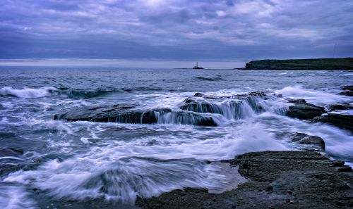 Free Powerful waves crash onto a rocky shoreline under a cloudy sky. Stock Photo
