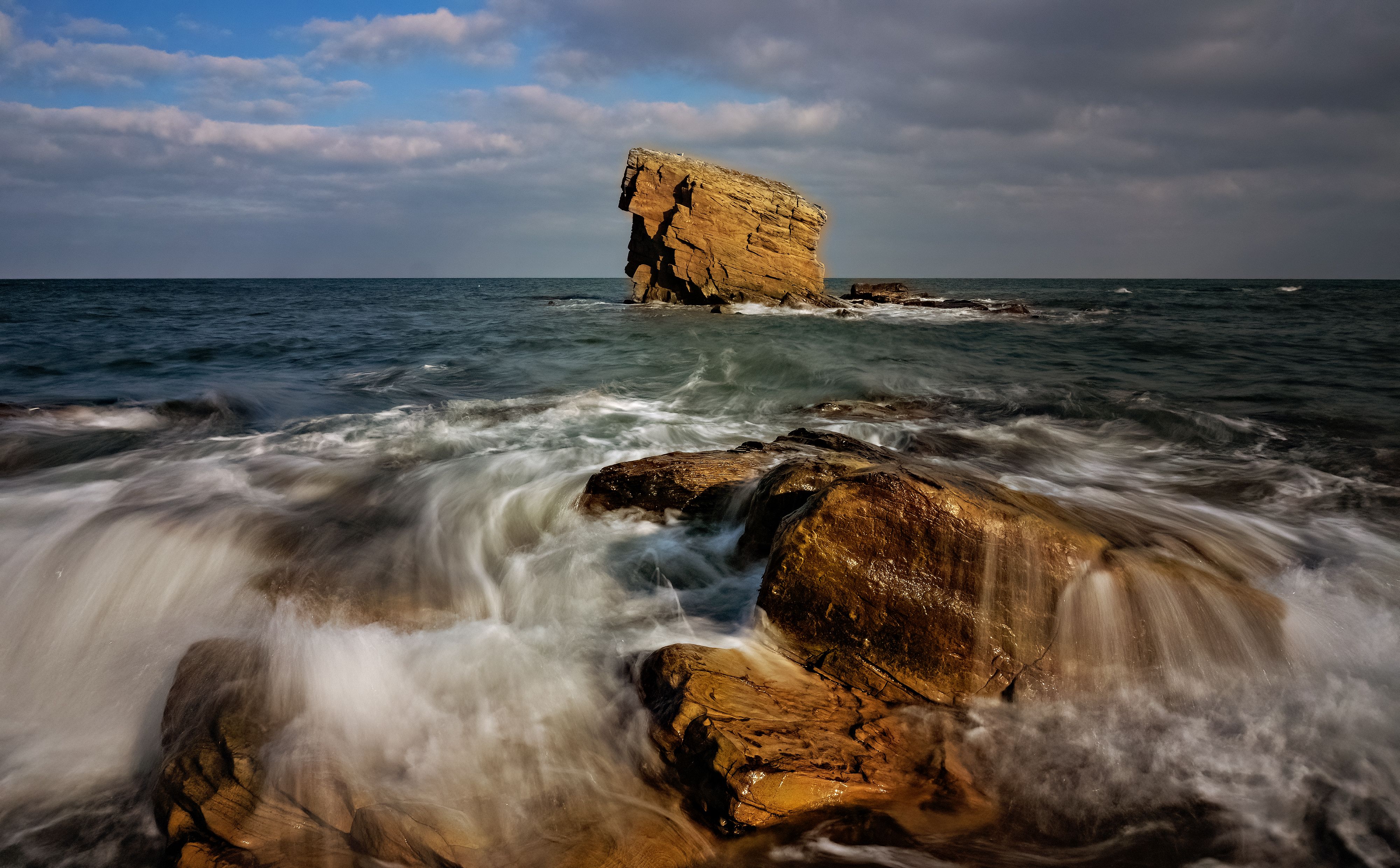 A rock formation in the ocean with waves crashing · Free Stock Photo
