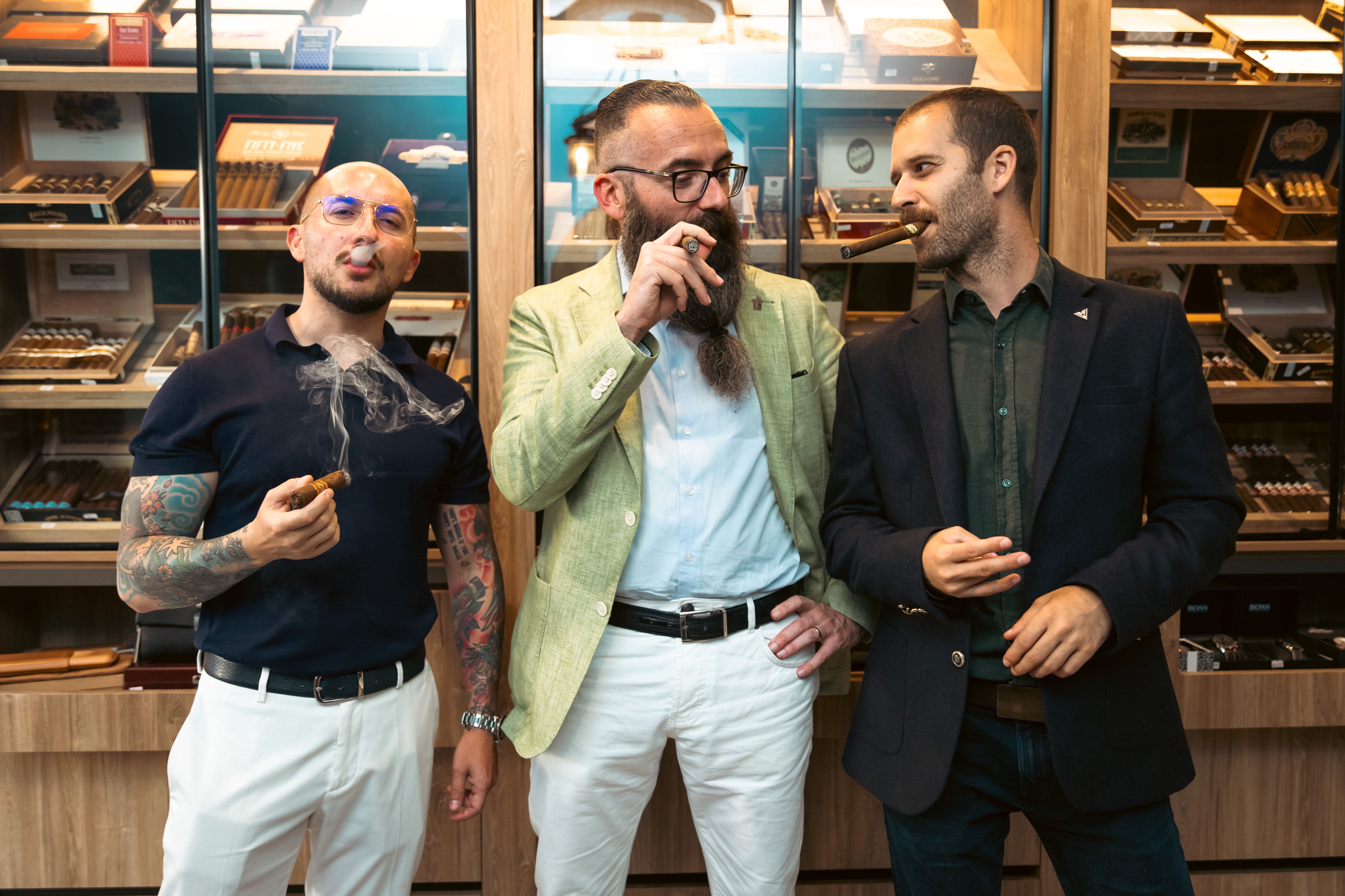 Three stylish men enjoying cigars in a modern cigar lounge, showcasing relaxed fashion.