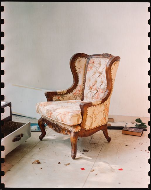 Vintage upholstered armchair in a dusty, abandoned space with scattered debris.