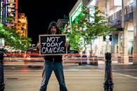 在繁忙的城市夜晚，一名男子举着抗癌标志，周围是灯光小径和建筑