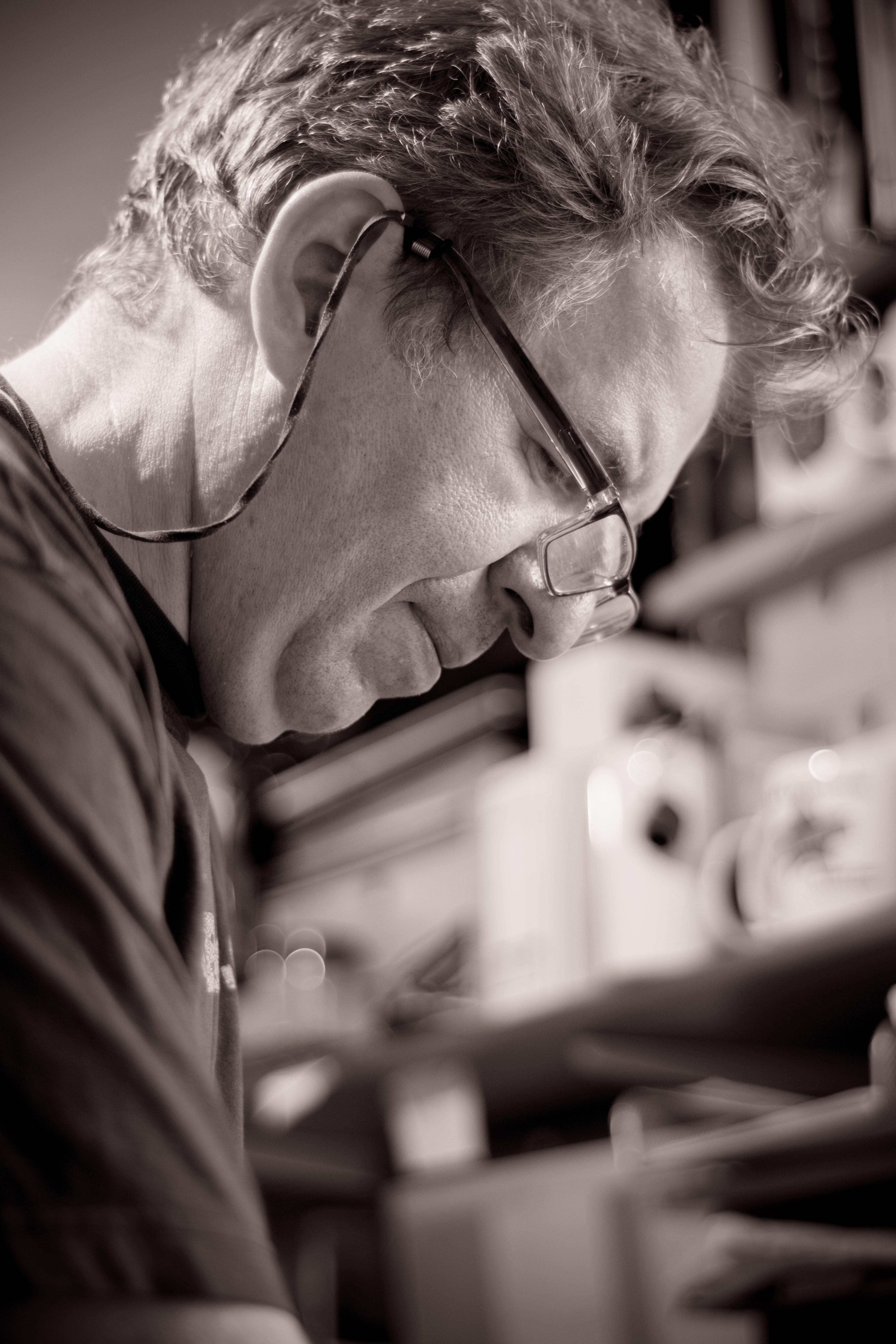 Adult man in glasses looking down, immersed in thought inside a study.