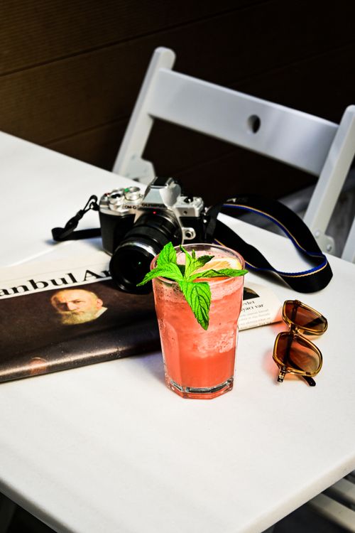 Free A refreshing pink cocktail on a table with a vintage camera, sunglasses, and a newspaper for a vacation vibe. Stock Photo