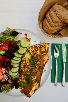 A close-up of a gourmet breakfast with omelette, fresh salad, and sliced bread on a white table.