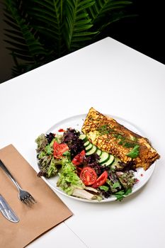 Delicious omelette served with a fresh salad on a white table indoors, perfect for a healthy meal.