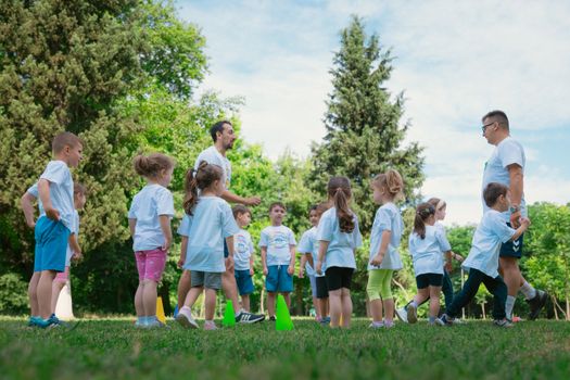 Group of children and teachers playing and learning in a sunny park setting.