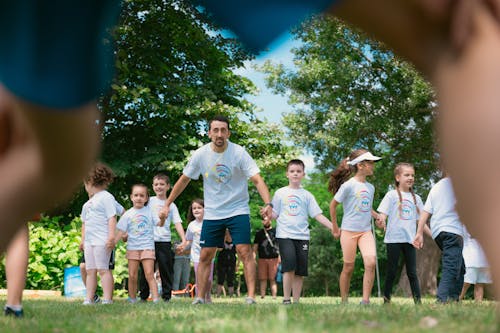 A group of children in white shirts and blue shorts are running in the grass