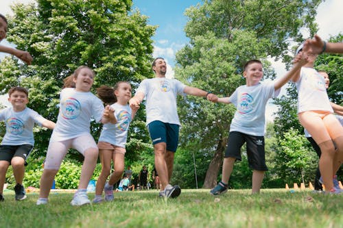 A group of children in white shirts and shorts are holding hands
