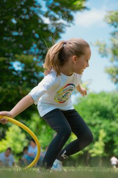 Energetic young girl enjoying playtime with a hula hoop in a sunny park setting.