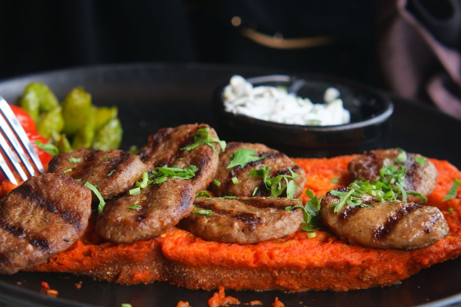 A plate of grilled ćevapi with kajmak and chopped onions, a classic Serbian dish.