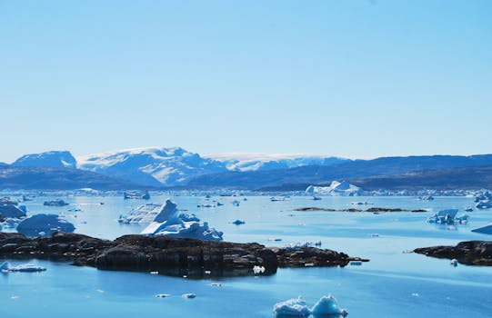 A breathtaking view of icebergs floating in a tranquil sea with distant snow-capped mountains, captured in Greenland.