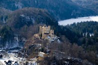 冬日阳光下，俯瞰一座历史悠久的城堡，周围是白雪皑皑的森林和群山环绕