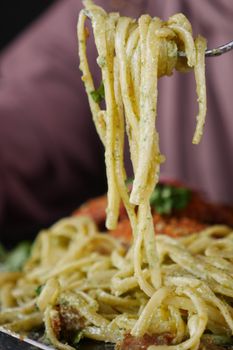 Close-up of fork twirling creamy Italian pasta with herbs.