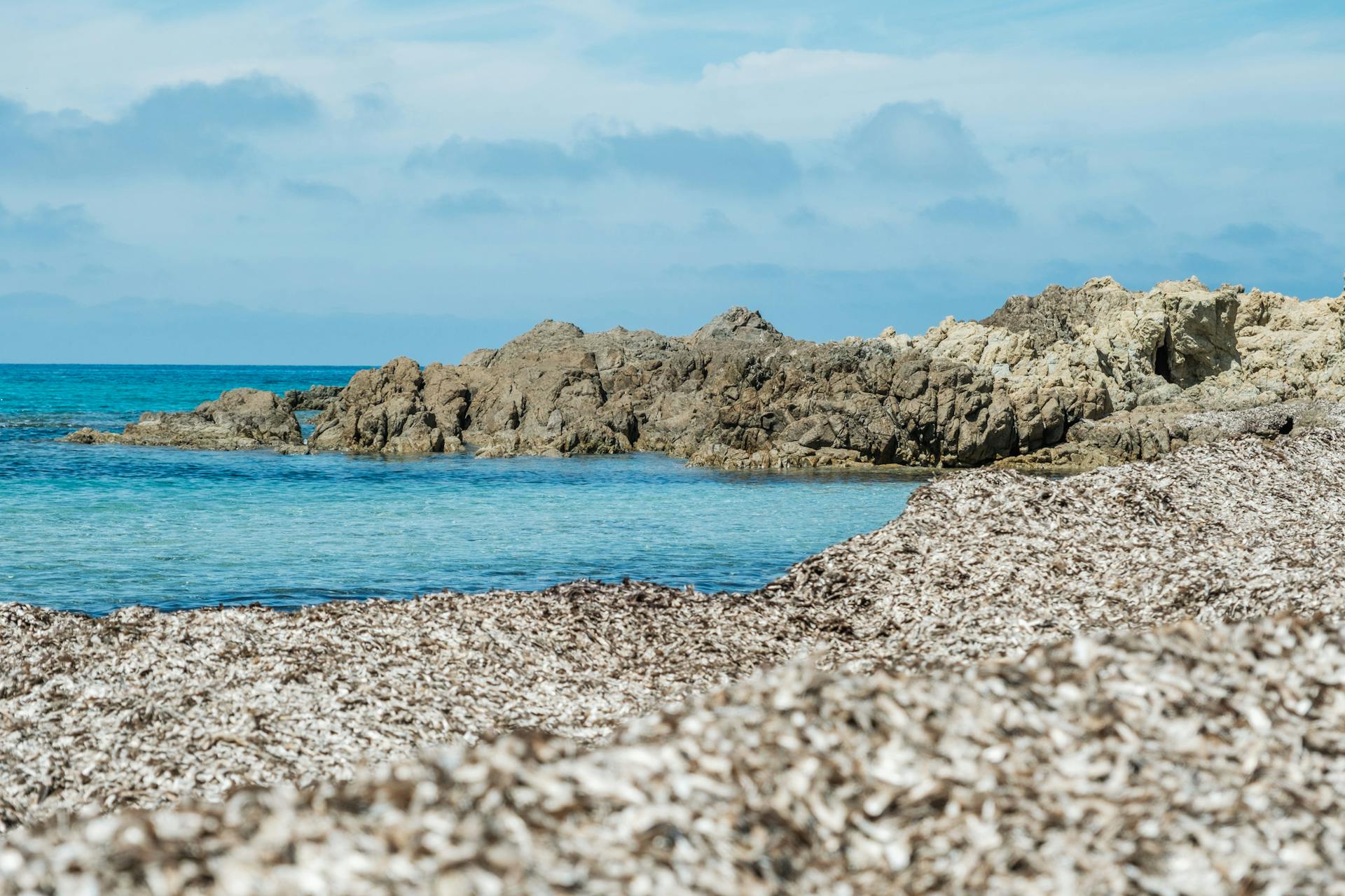 Scenic view of the rocky coastline in Palasca, Corsica with clear blue waters and bright sky.