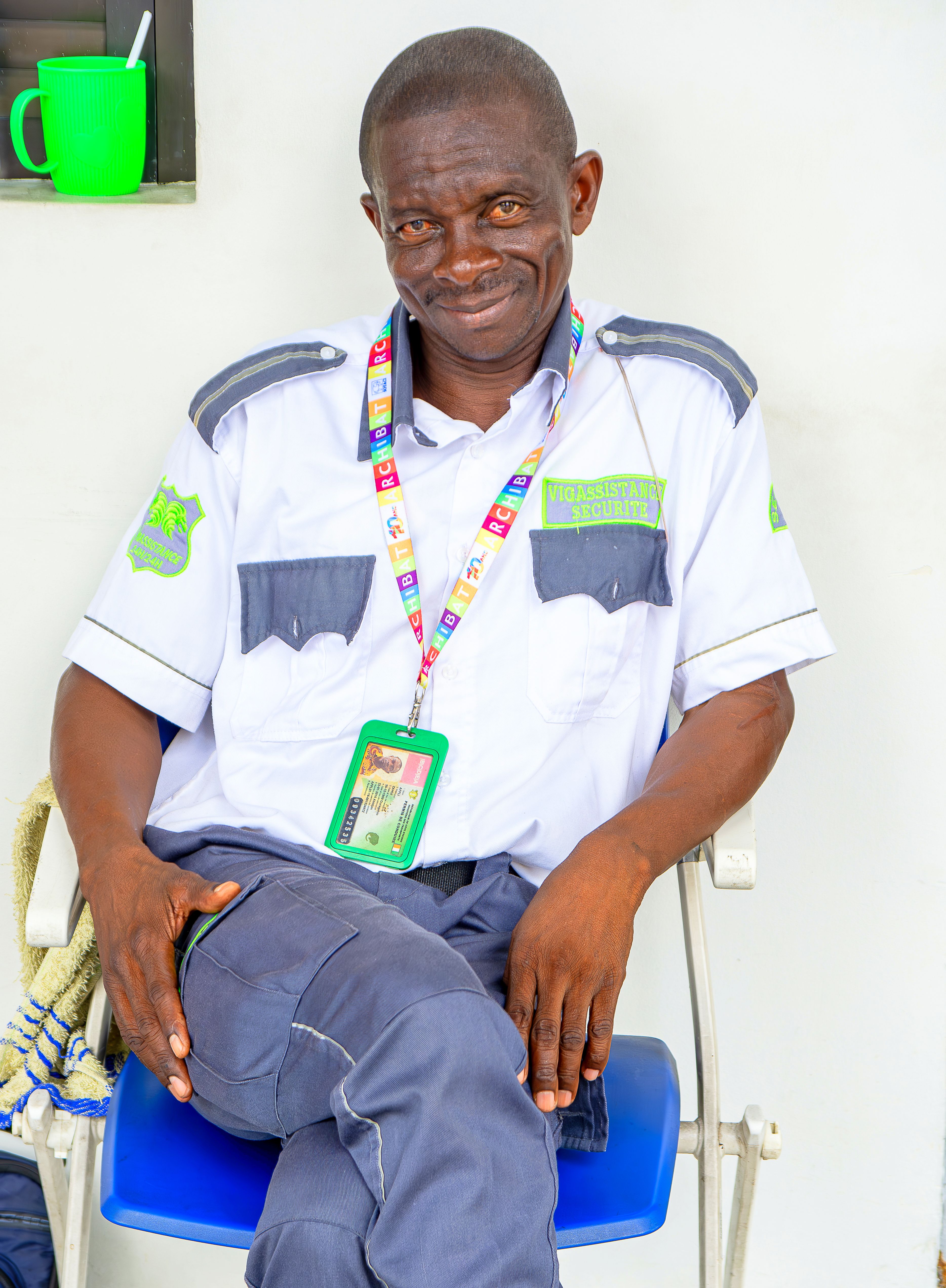 Portrait of a smiling security guard seated on a chair in uniform indoors.