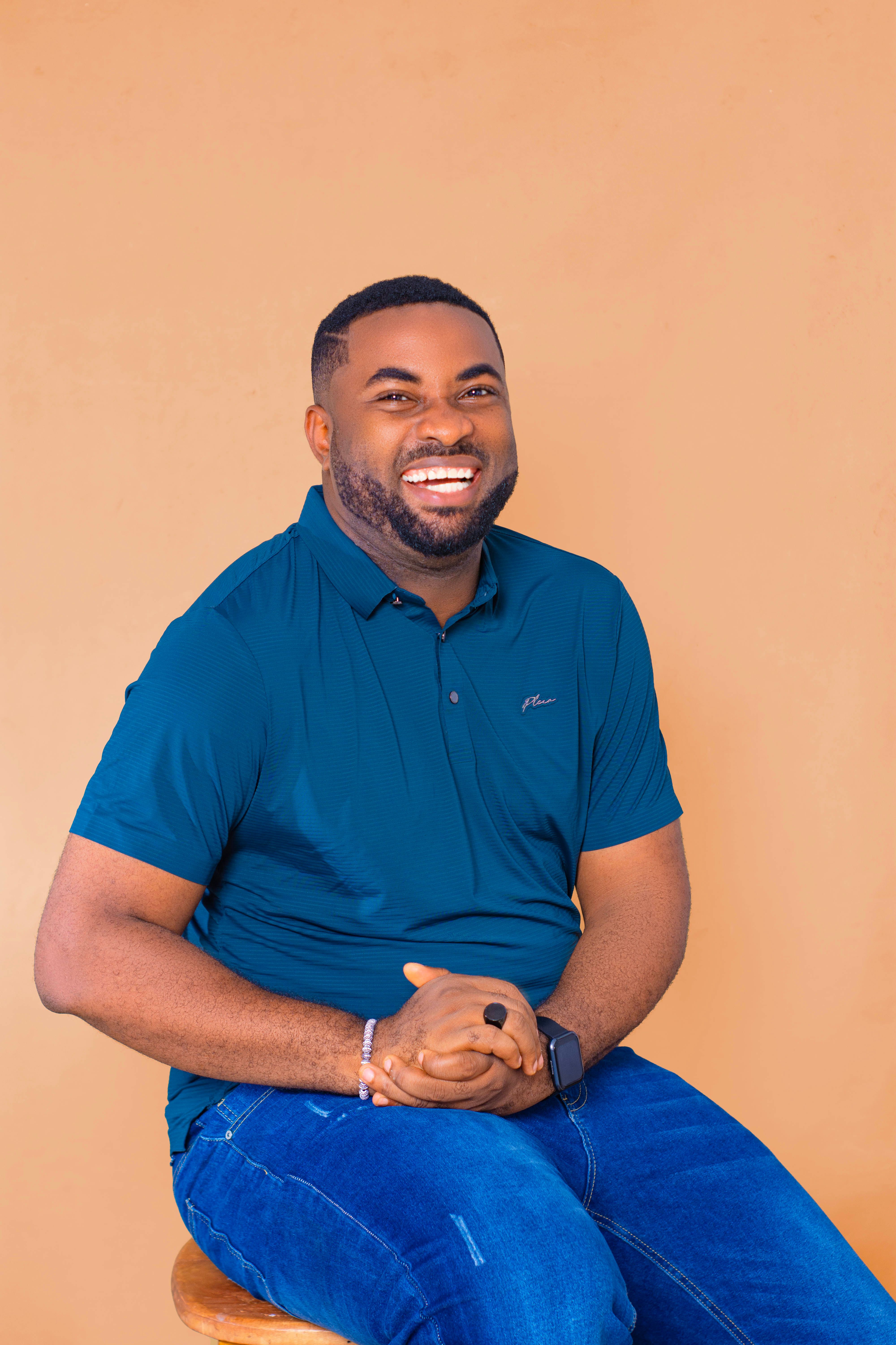 Portrait of a joyful man sitting while wearing a blue polo and jeans in a studio setup.