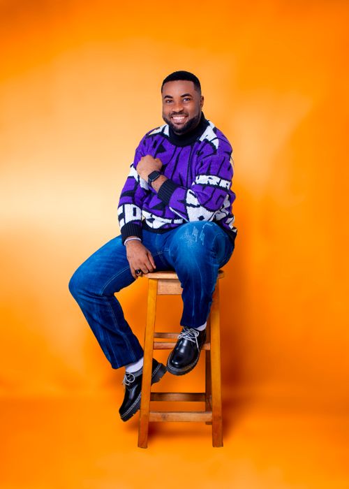 Free Studio portrait of a man sitting on a stool, wearing a stylish sweater against a vibrant yellow background. Stock Photo