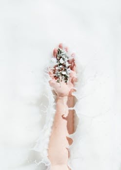 一只握着鲜花的手优雅地从舒缓的牛奶浴中伸出，尽显现代极简主义风格