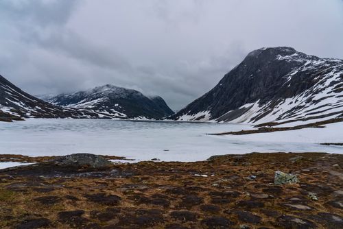 Free A serene view of a frozen lake amidst snow-covered mountains and a cloudy sky. Stock Photo