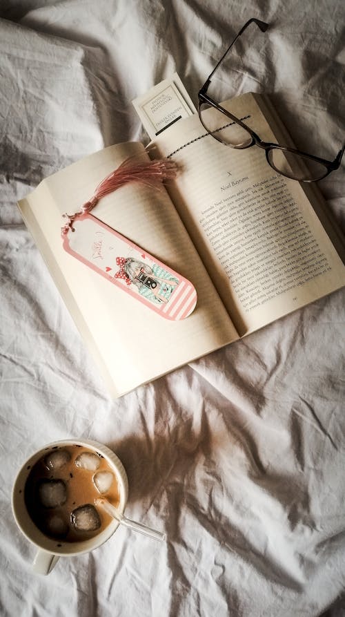 A book, glasses and a cup of coffee on a bed