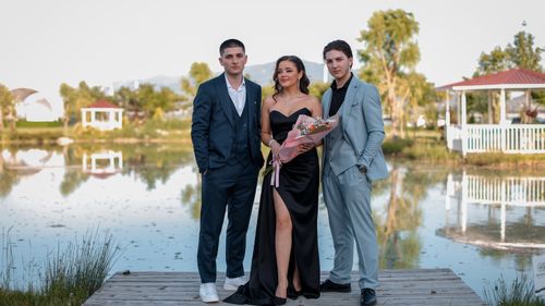 Free Three elegantly dressed adults pose by a peaceful lakeshore, perfect for fashion or event themes. Stock Photo
