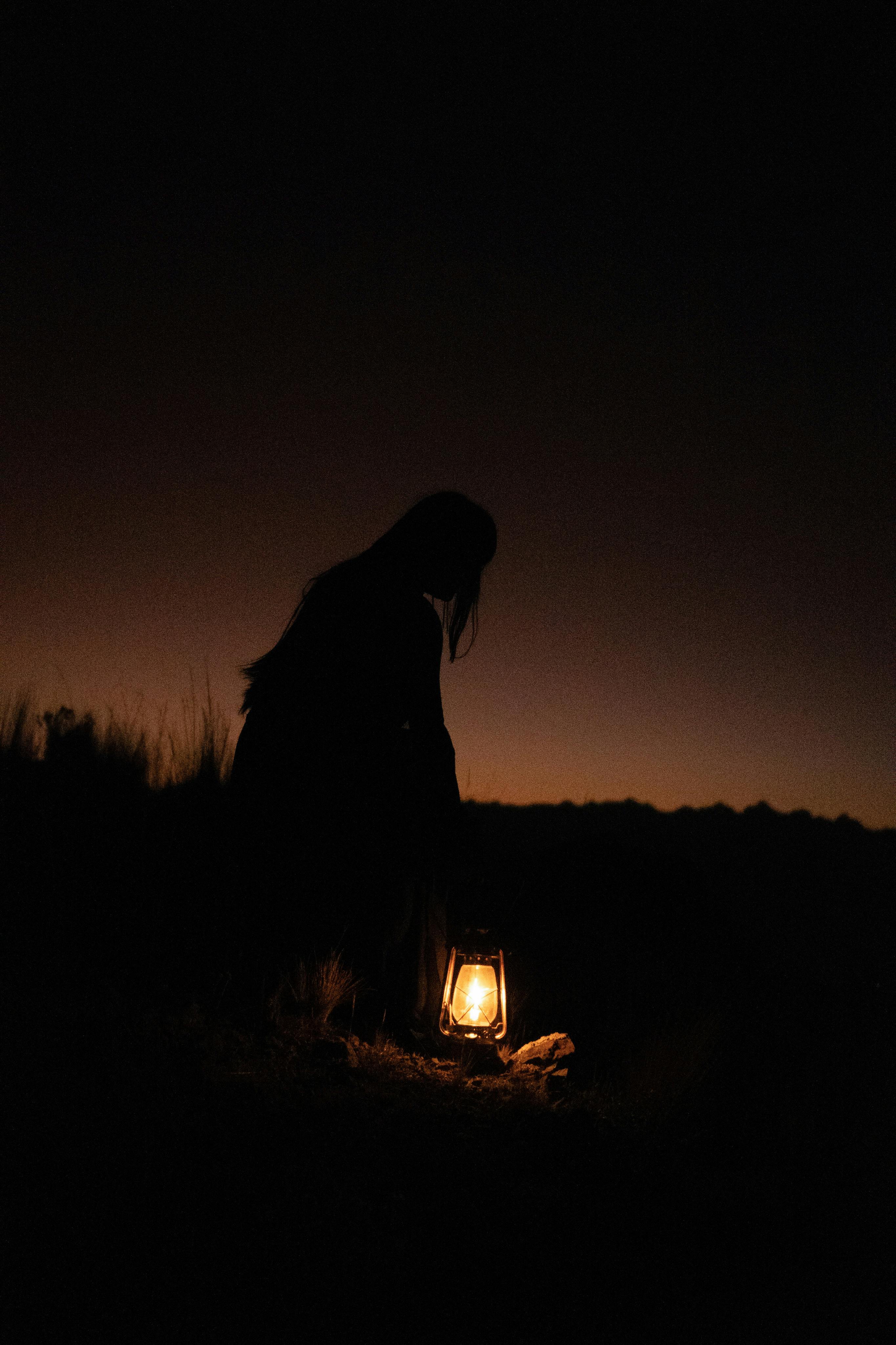 A figure holds a glowing lantern in a dark field under a night sky in Cusco, Peru.