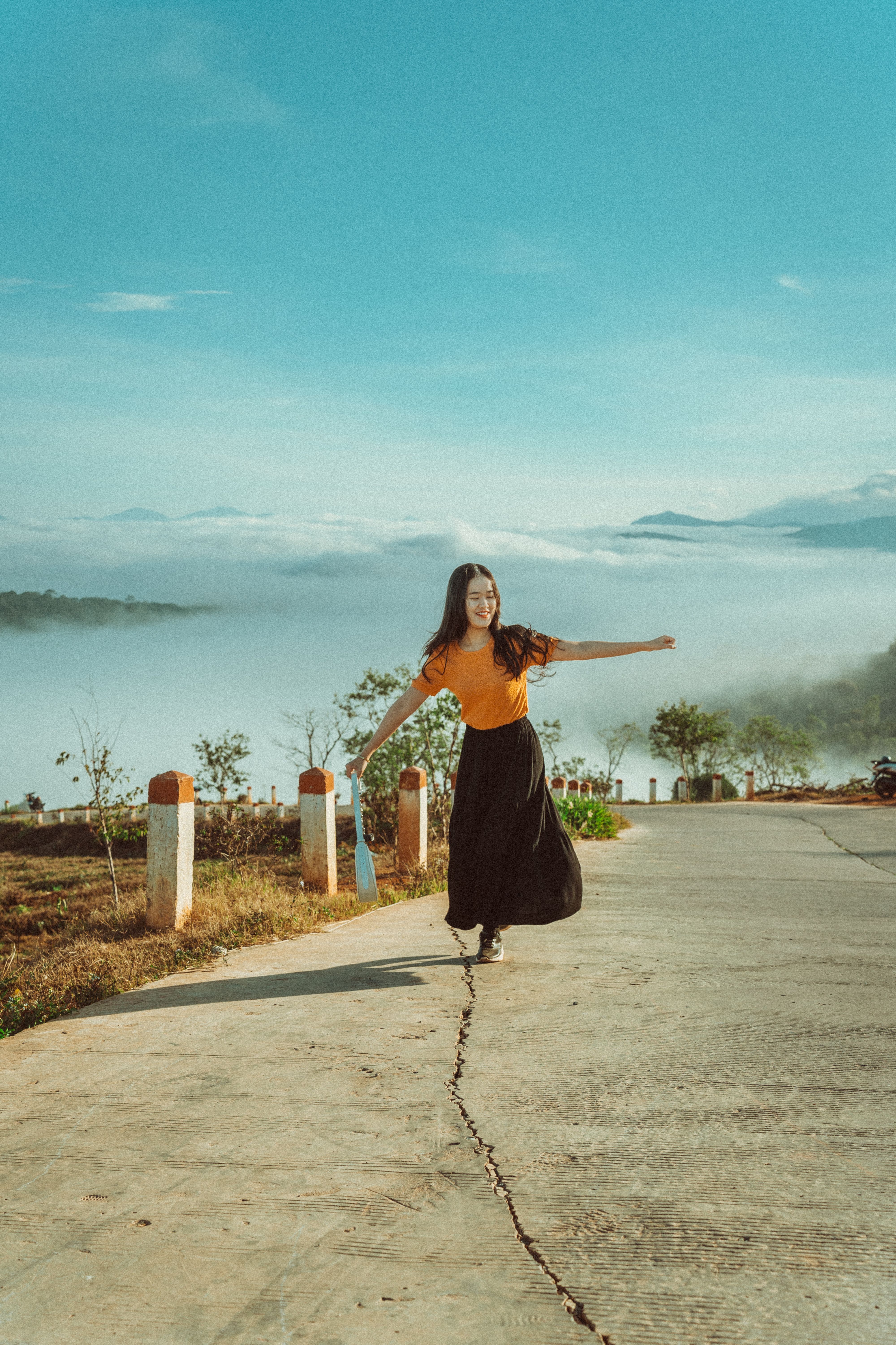 A smiling woman gracefully balances on a rural road in Dalat, Vietnam, surrounded by scenic hills and mist.