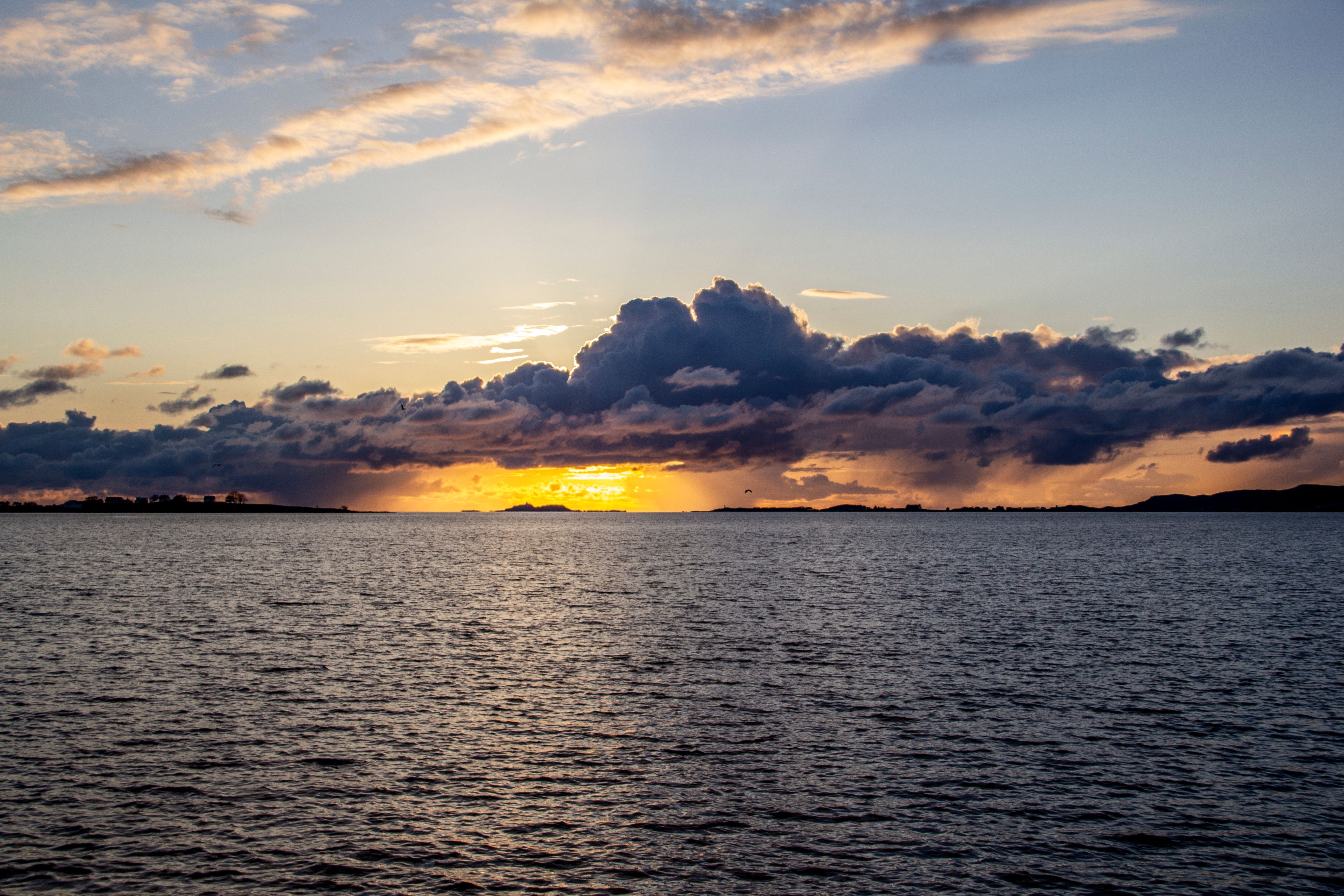 A sunset over the water with clouds in the sky