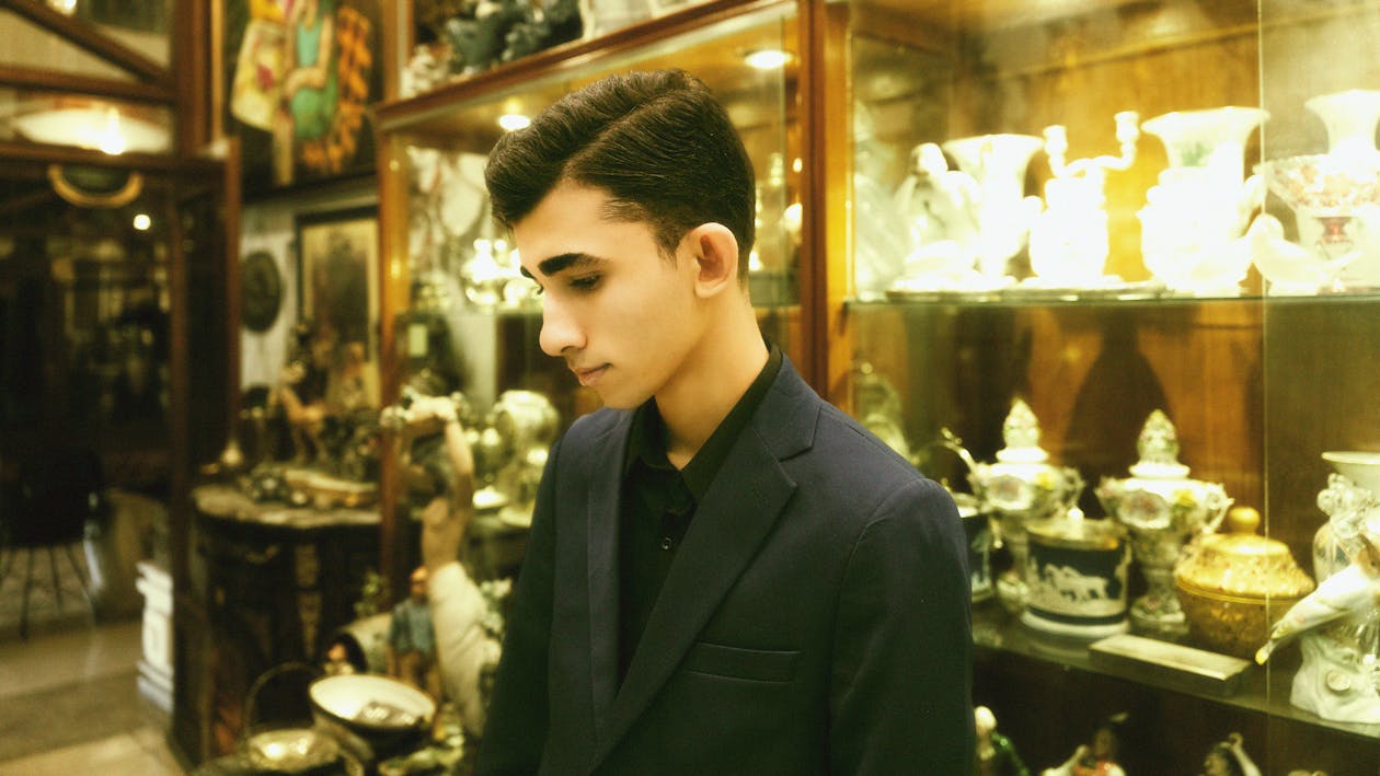 A young man in a suit standing in front of a display of antiques