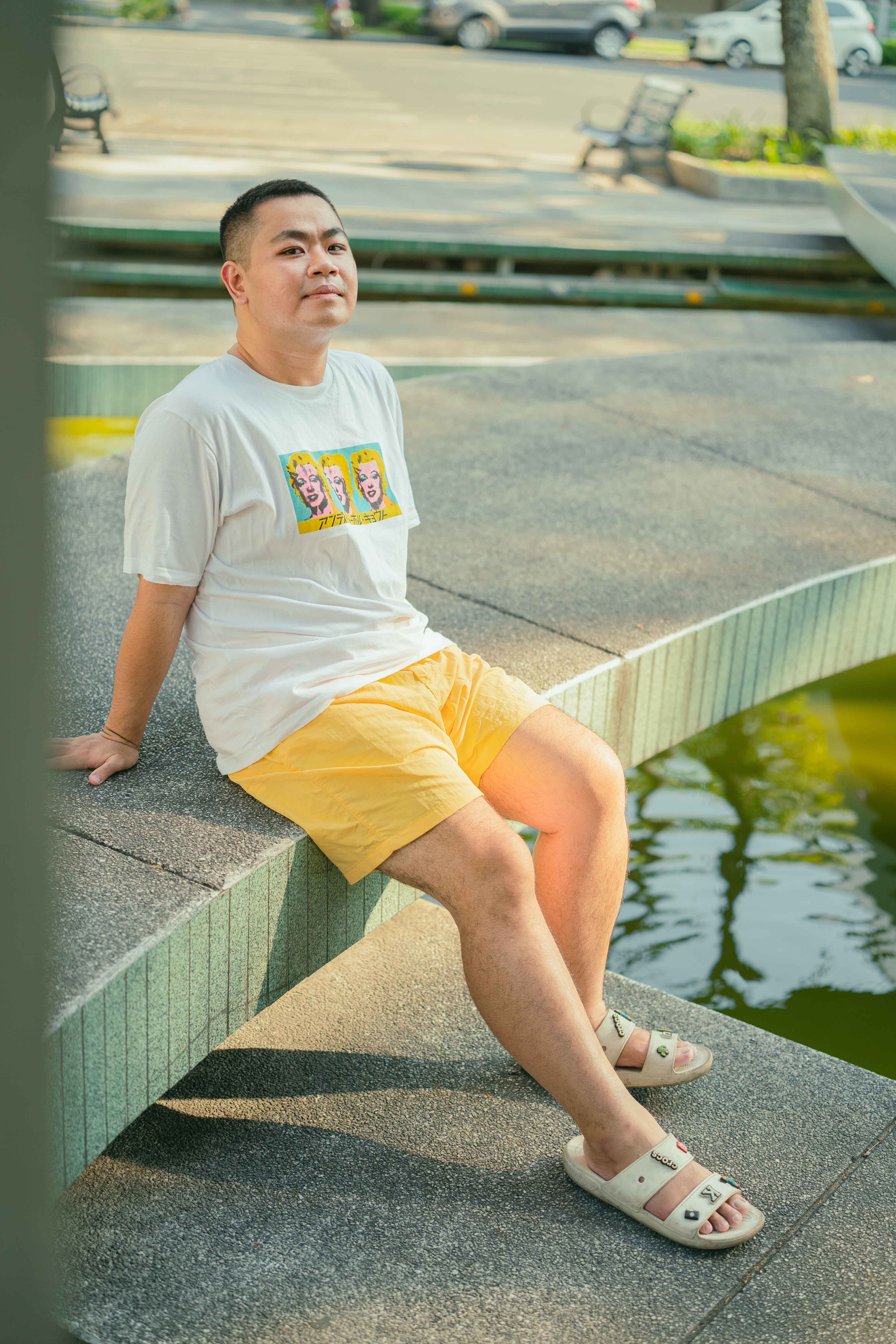 Man sitting on a wall in a park in Ho Chi Minh City, enjoying a sunny day outdoors.