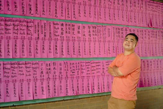 Smiling man standing in front of a vibrant wall of names in Ho Chi Minh City.