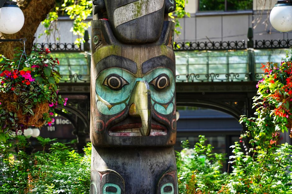 Detailed image of a colorful totem pole surrounded by lush greenery in a vibrant outdoor setting.