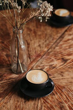 一张质朴的木桌上放着一杯温暖的卡布奇诺，旁边有个装饰花瓶，营造出舒适的氛围